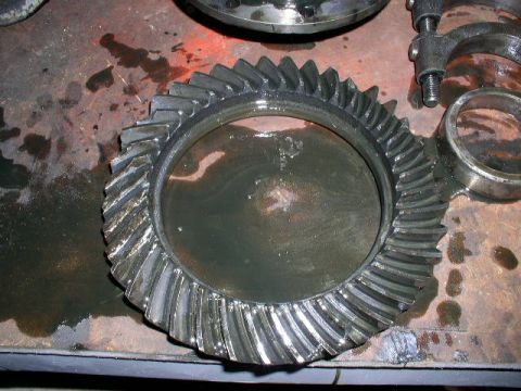 1979 Ford Bronco - A differential ring gear with visible damage to its teeth sits on a stained workbench, alongside other disassembled parts.