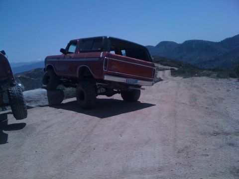 1978 Ford Bronco - A lifted red 1978 Ford Bronco is parked on a rocky mountain road with another vehicle to its left.