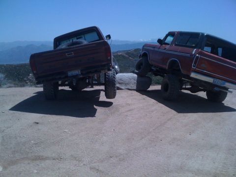 1978 Ford Bronco - Two lifted trucks, a 1978 Ford Bronco and a pickup, navigate a rocky dirt path with a mountainous vista.