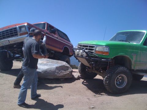 1978 Ford Bronco - Two modified Broncos are positioned on a rocky terrain under a clear blue sky.