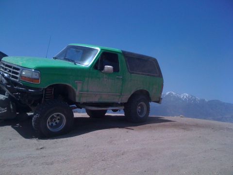 1978 Ford Bronco - A lifted green Ford Bronco sits on a dusty trail with mountains in the background.