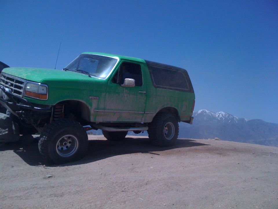Green Ford Bronco with aftermarket bumper and lift kit on a dirt road