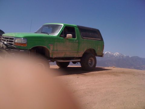1978 Ford Bronco - This green SUV with a black top is parked on a dirt hill with mountains in the distance.