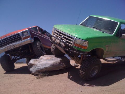 1978 Ford Bronco - Two modified Ford trucks navigate a rocky obstacle course under a clear blue sky.
