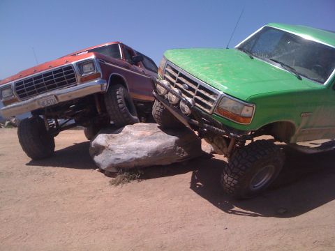 1978 Ford Bronco - Two modified trucks, a red Bronco and a green F-series, navigate rocky terrain under a clear blue sky.