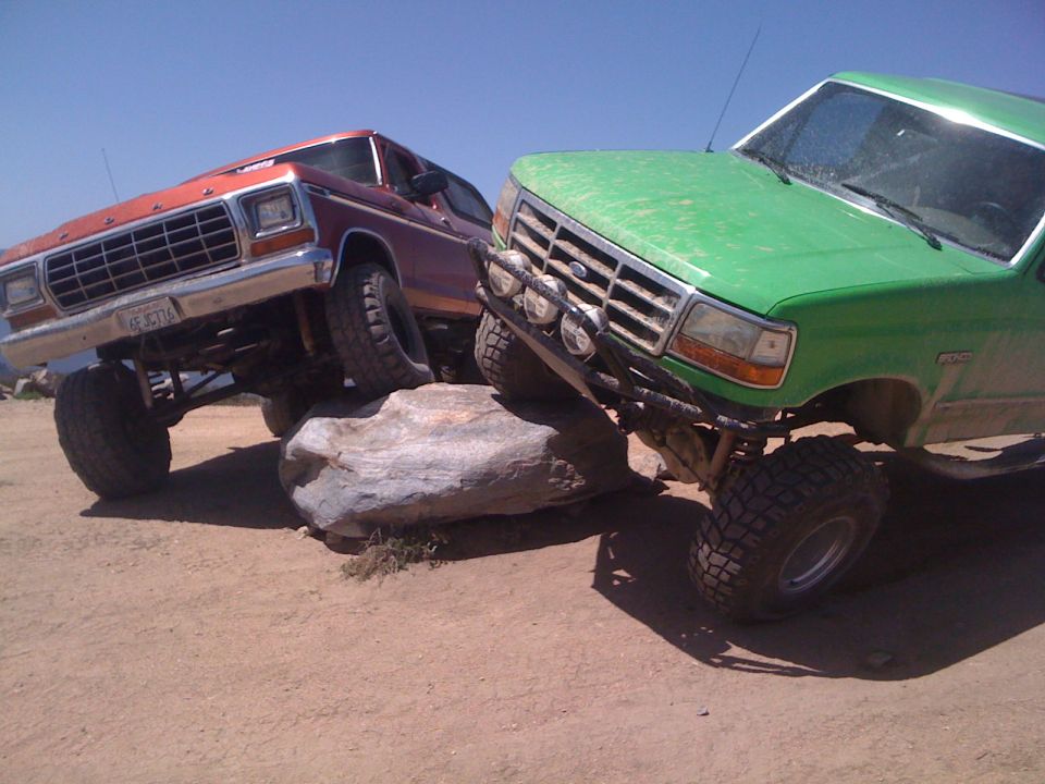 Red 1980s Ford Bronco and green Ford F-series truck on rocks