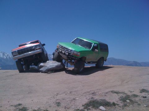 1978 Ford Bronco - Two modified Ford SUVs navigate a rocky trail under a clear blue sky.