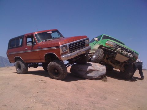 1978 Ford Bronco - Two modified trucks navigate a rocky obstacle course under a clear blue sky.