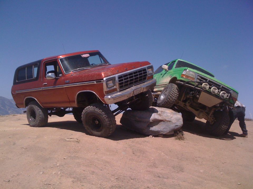 Orange Bronco and green truck climbing rocks. Bronco has a 1978 grille