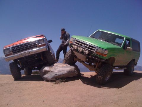 1978 Ford Bronco - Two modified SUVs are positioned on large rocks under a clear blue sky.