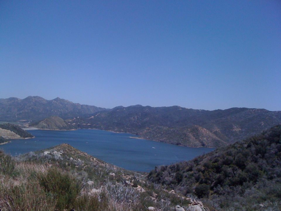 Lake surrounded by mountains under a clear blue sky. Some dry brush in the foreground