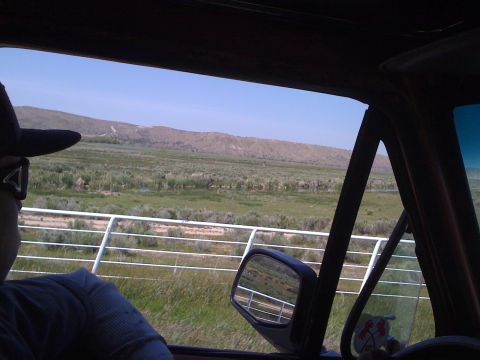 1978 Ford Bronco - View from inside a vehicle traveling through a scenic rural area, with mountains in the distance and a fence line along the roadside.