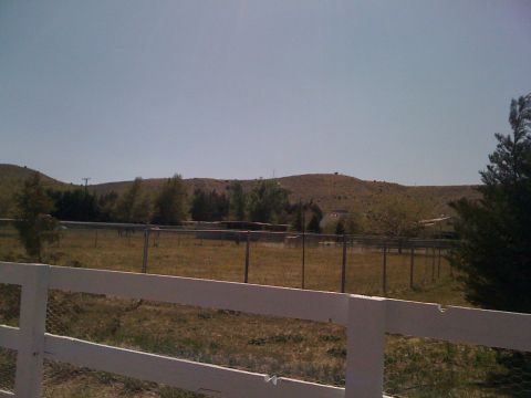 1978 Ford Bronco - A wide view of a rural property shows a white fence, a fenced field with trees, and rolling hills in the distance.