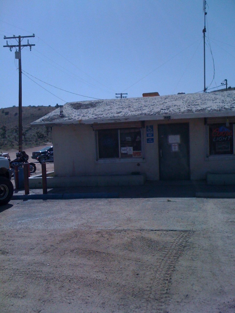 Building with a Coors Light sign, parked motorcycles, and a white vehicle's front fender