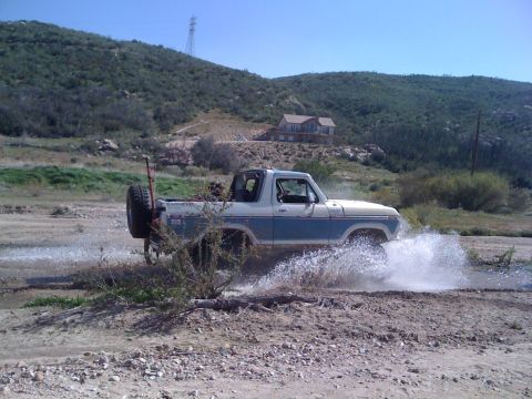 1978 Ford Bronco - A classic Ford Bronco navigates a watery path, creating a significant splash.