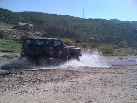 1978 Ford Bronco - 1978 Ford Bronco splashes through a water crossing in a dry, hilly landscape.