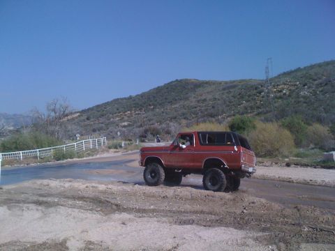 1978 Ford Bronco - A red 1978 Ford Bronco navigates a dusty, off-road path with hills in the background.