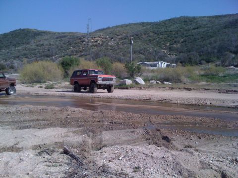 1978 Ford Bronco - A red 1978 Ford Bronco navigates a muddy terrain, with another vehicle visible in the background.
