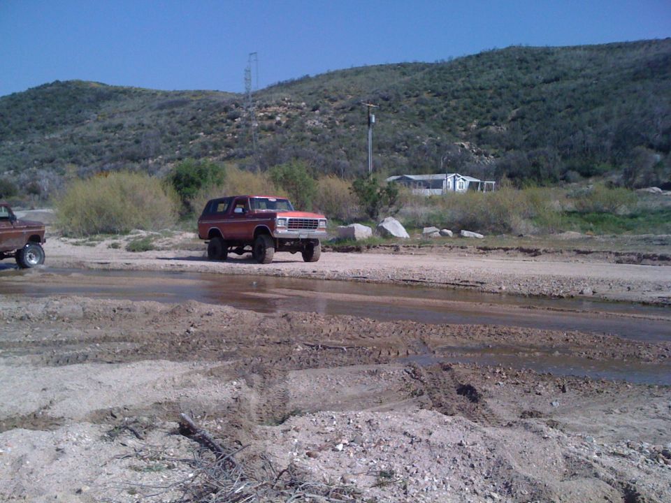 Red 1978 Ford Bronco driving through mud