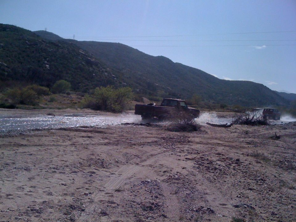 Red pickup truck driving through shallow water, another vehicle in background