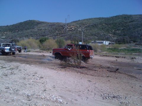 1978 Ford Bronco - A red 1978 Ford Bronco navigates a muddy, watery terrain with other vehicles present.