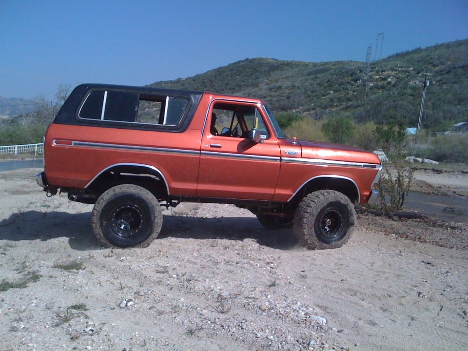 Orange 1978 Ford Bronco side view with black top and off-road tires