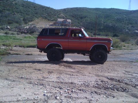 1978 Ford Bronco - This lifted 1978 Ford Bronco navigates a dirt and water path in a dry, hilly landscape.