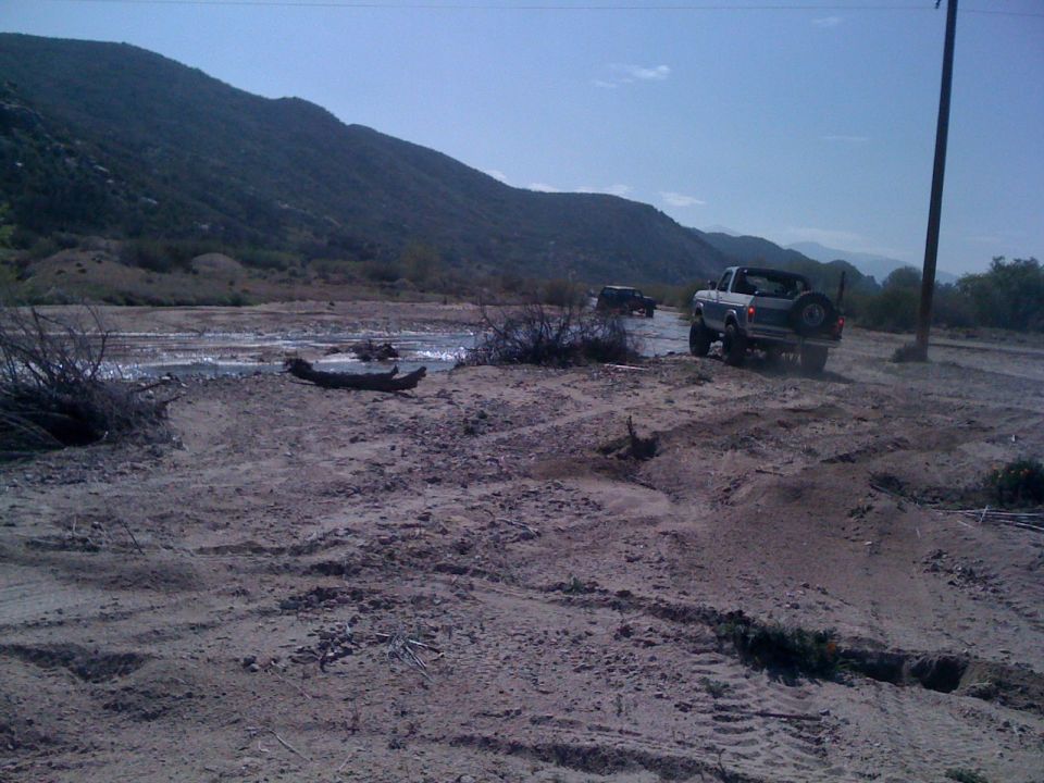 Silver 1978 Ford Bronco driving on a dirt path with a second vehicle behind it