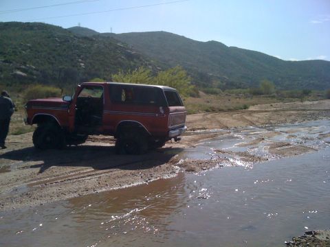 1978 Ford Bronco - A red 1978 Ford Bronco is seen off-road with its doors open, navigating a wet, muddy terrain.
