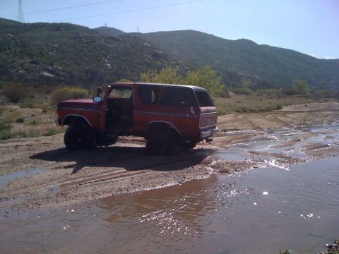 1978 Ford Bronco - This red 1978 Ford Bronco navigates a muddy terrain with its door ajar.