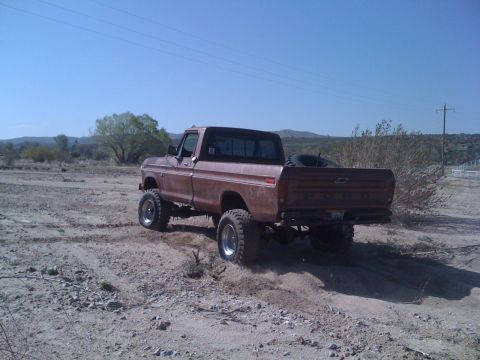 1978 Ford Bronco - Lifted 1977 Ford F-150 pickup truck navigates a dusty off-road trail under a clear blue sky.