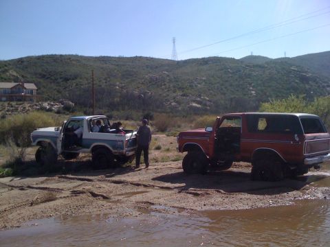 1978 Ford Bronco - Two Ford Broncos are parked in a muddy area with people inside and around them.
