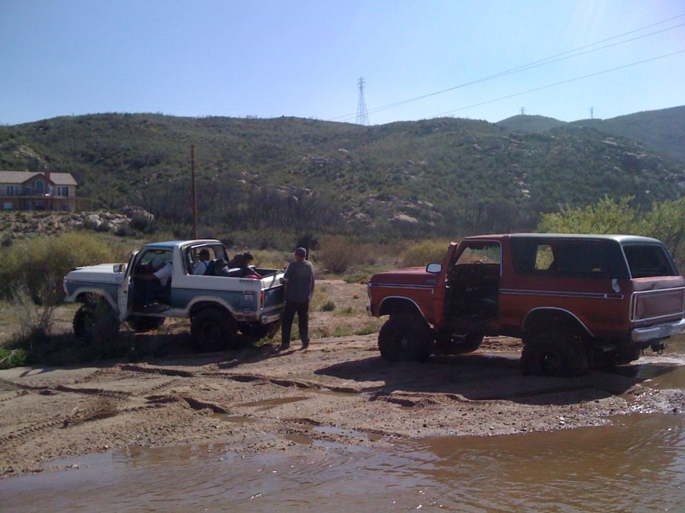 Two 1978 Ford Broncos parked in a muddy, outdoor area with hills in the background