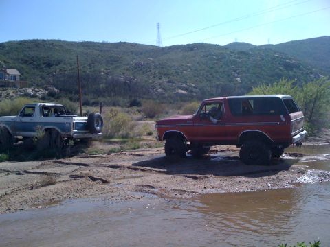 1978 Ford Bronco - Two Ford Broncos navigate a muddy terrain, with one vehicle assisting the other.