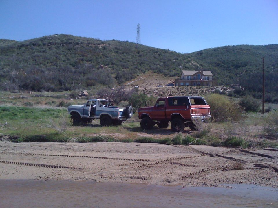 Two 1978 Ford Broncos parked in a dry, grassy area with tire tracks in the foreground