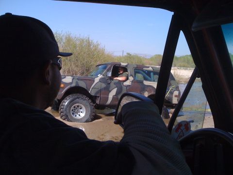1978 Ford Bronco - A camouflage SUV navigates through a muddy terrain, with another vehicle's interior visible in the foreground.