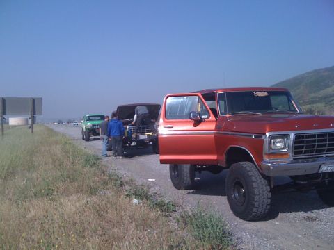 1978 Ford Bronco - Several vehicles, including an orange 1978 Ford Bronco, are parked on the side of a road under a clear blue sky.