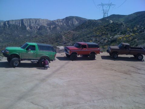 1978 Ford Bronco - A red 1978 Ford Bronco is parked alongside a green Bronco and a brown pickup truck in a desert landscape.