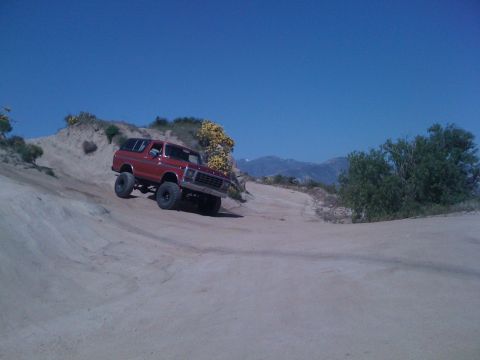 1978 Ford Bronco - A red 1978 Ford Bronco navigates a dusty off-road trail under a clear blue sky.