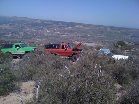 1978 Ford Bronco - Three SUVs are parked in a dry, hilly landscape, with the orange Bronco's hood open.