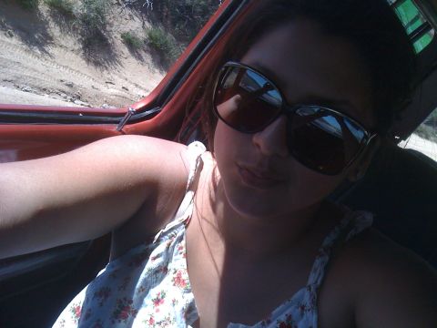 1978 Ford Bronco - A woman wearing sunglasses and a floral top takes a selfie from inside a red vehicle.