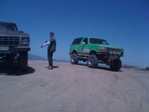 1978 Ford Bronco - Two modified SUVs are parked on a dirt hill under a clear blue sky.