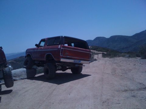 1978 Ford Bronco - A red 1978 Ford Bronco is parked on a dirt road with mountains in the background.