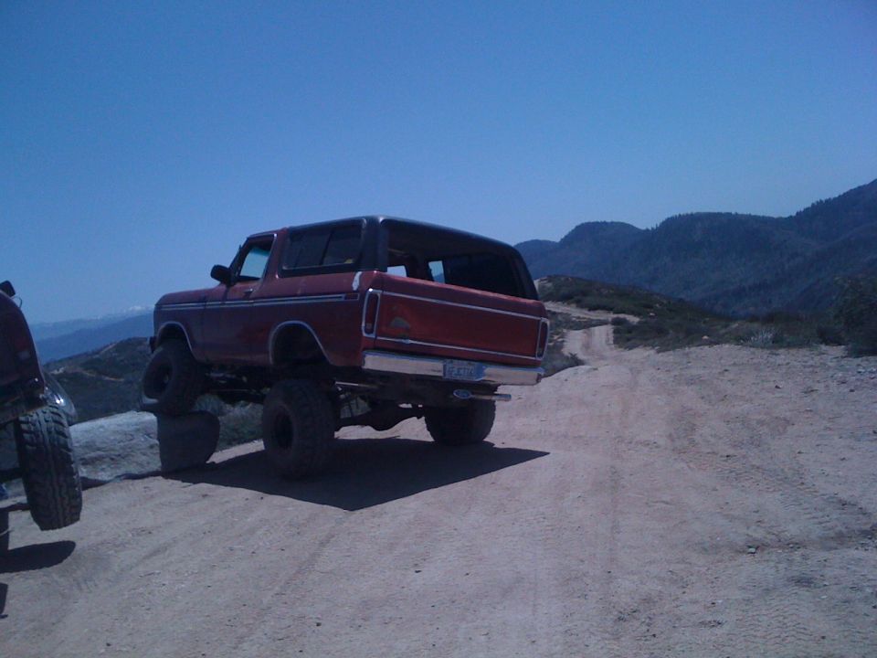 Red 1978 Ford Bronco with black top, lifted suspension, and large tires on a dirt road