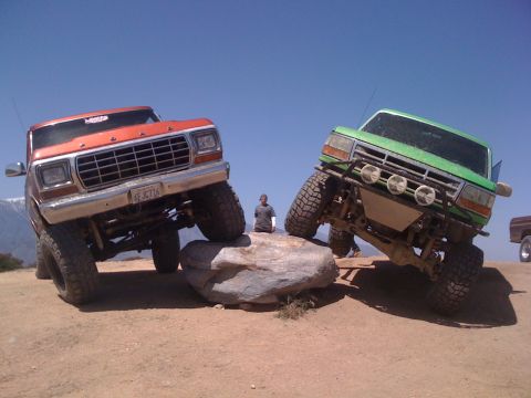 1978 Ford Bronco - Two modified trucks are navigating an obstacle course on a sunny day.