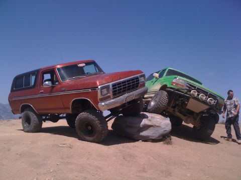 1978 Ford Bronco - A red 1978 Ford Bronco and a green off-road truck are positioned on rocks under a clear blue sky.