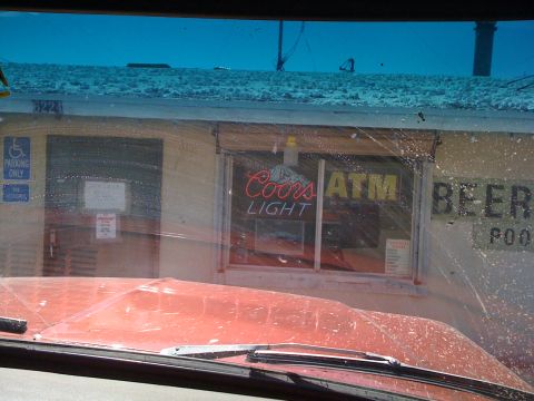 1978 Ford Bronco - View from inside a red vehicle looking out at a store with neon signs for Coors Light, ATM, and Beer.