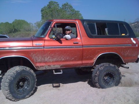 1978 Ford Bronco - Side view of a 1978 Ford Bronco with a driver, lifted suspension, and off-road tires.
