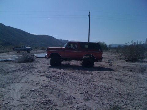 1978 Ford Bronco - A red 1978 Ford Bronco sits in a desert landscape next to a utility pole, with another vehicle in the background.
