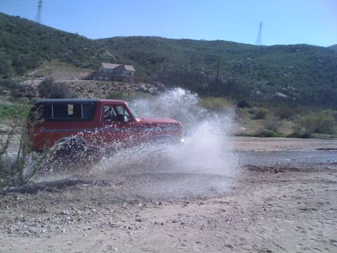 1978 Ford Bronco - A red 1978 Ford Bronco navigates through a watery terrain, creating a significant splash.